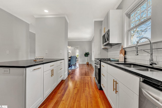 kitchen with appliances with stainless steel finishes, ornamental molding, sink, white cabinets, and light hardwood / wood-style floors