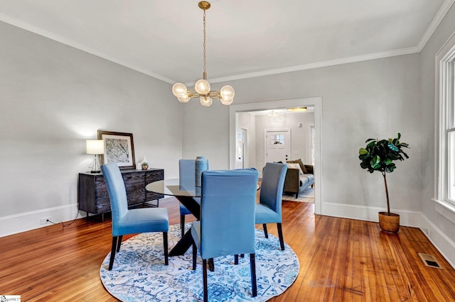 dining space featuring hardwood / wood-style flooring, crown molding, and an inviting chandelier