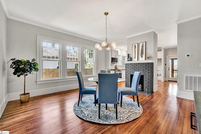 dining space featuring crown molding, dark hardwood / wood-style flooring, a fireplace, and an inviting chandelier