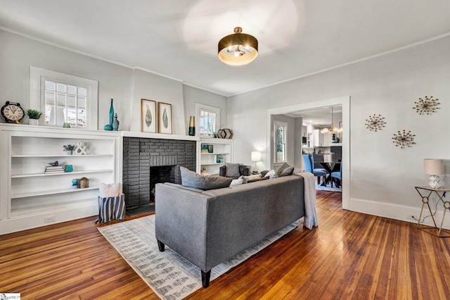 living room featuring built in shelves, hardwood / wood-style flooring, and a brick fireplace