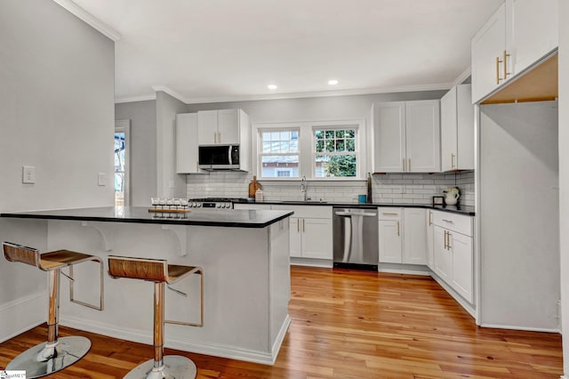 kitchen with kitchen peninsula, light wood-type flooring, stainless steel appliances, white cabinetry, and a breakfast bar area