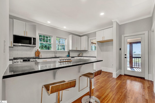 kitchen with white cabinets, crown molding, sink, light hardwood / wood-style floors, and a breakfast bar area