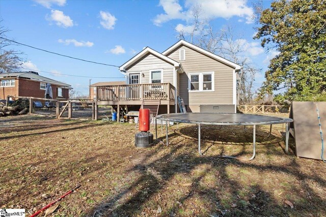 rear view of property featuring a trampoline and a wooden deck