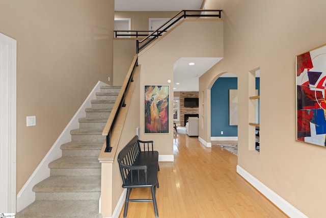 staircase featuring a high ceiling, hardwood / wood-style flooring, and a stone fireplace