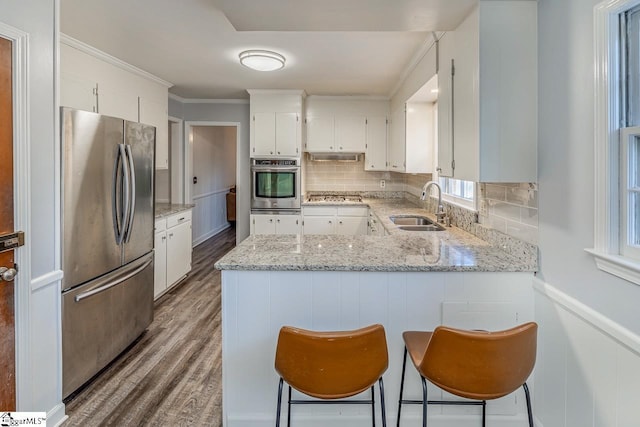 kitchen featuring white cabinets, sink, light stone countertops, kitchen peninsula, and stainless steel appliances