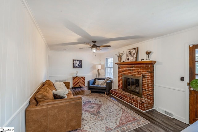 living room featuring ceiling fan, crown molding, a fireplace, and dark wood-type flooring