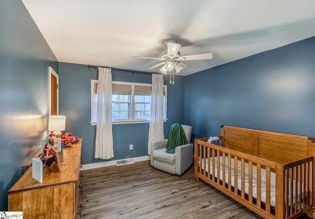 bedroom featuring hardwood / wood-style floors, ceiling fan, and a nursery area