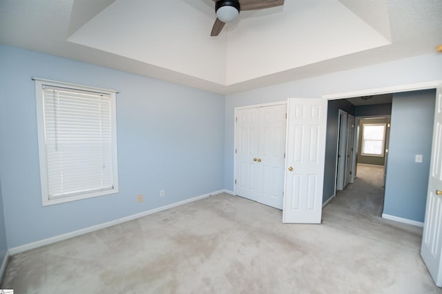 unfurnished bedroom featuring ceiling fan, a raised ceiling, light carpet, and a closet