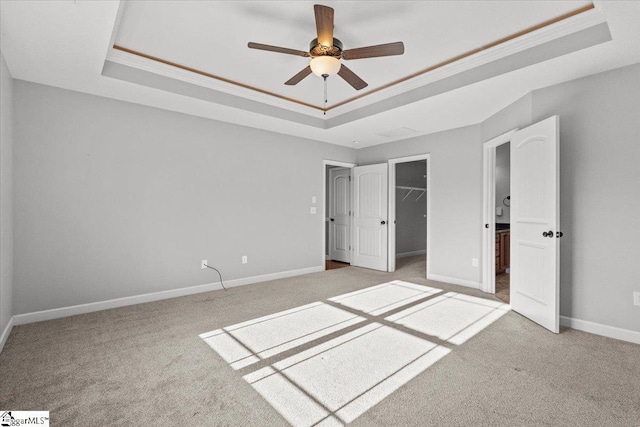 unfurnished bedroom featuring a walk in closet, ceiling fan, ornamental molding, a tray ceiling, and a closet