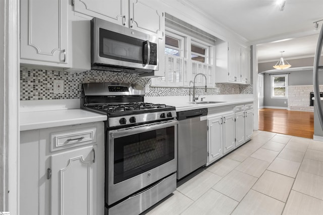 kitchen with pendant lighting, white cabinets, crown molding, sink, and appliances with stainless steel finishes