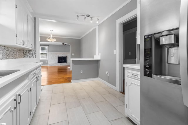 kitchen featuring stainless steel refrigerator with ice dispenser, a brick fireplace, crown molding, decorative light fixtures, and white cabinetry