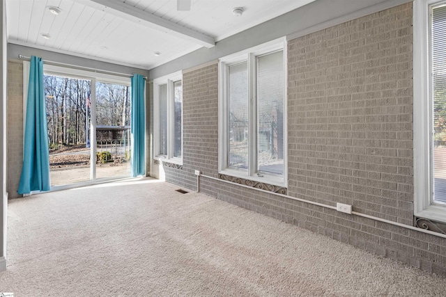 empty room with carpet flooring, beam ceiling, and brick wall