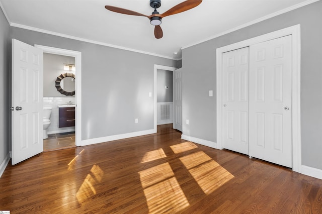 unfurnished bedroom featuring ensuite bathroom, ornamental molding, ceiling fan, dark wood-type flooring, and a closet