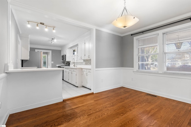 kitchen featuring white cabinets, ornamental molding, appliances with stainless steel finishes, and light hardwood / wood-style flooring