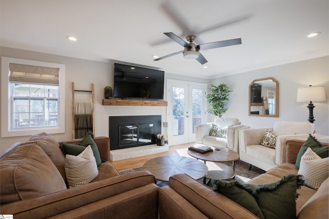 living room featuring ceiling fan, french doors, a brick fireplace, crown molding, and light hardwood / wood-style floors