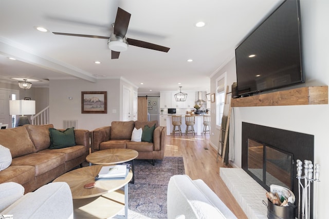 living room with a barn door, light hardwood / wood-style flooring, ceiling fan, and crown molding