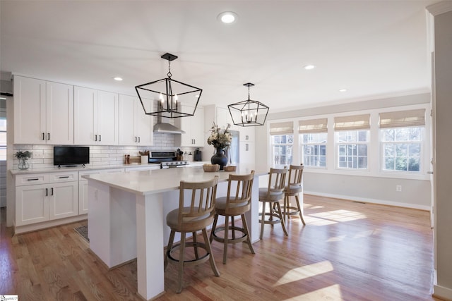 kitchen with ventilation hood, decorative light fixtures, a kitchen island, white cabinetry, and a breakfast bar area