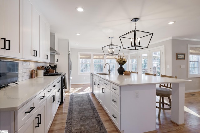 kitchen with white cabinetry, sink, hanging light fixtures, stainless steel appliances, and a large island with sink