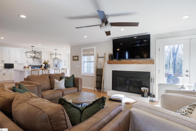 living room featuring ceiling fan with notable chandelier, light wood-type flooring, ornamental molding, and a wealth of natural light