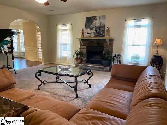 living room featuring a stone fireplace and ceiling fan