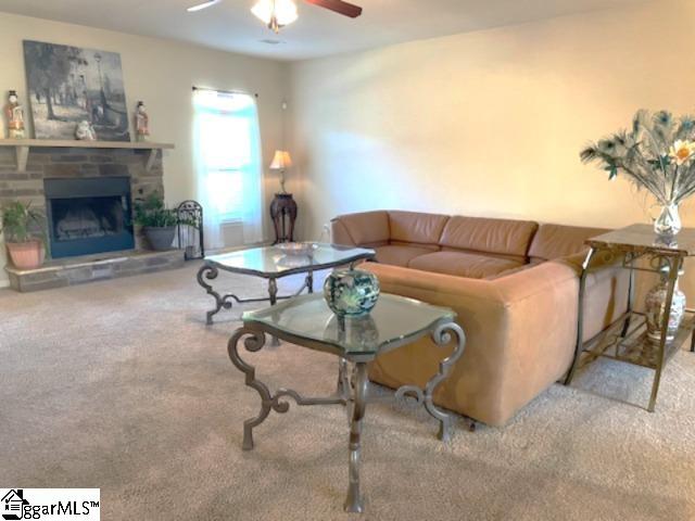 carpeted living room featuring ceiling fan and a stone fireplace