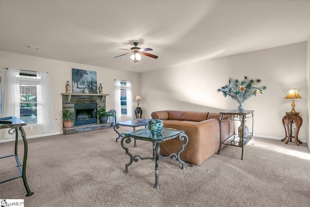 carpeted living room with ceiling fan and a stone fireplace