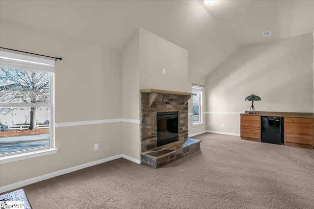 carpeted living room with a stone fireplace and lofted ceiling