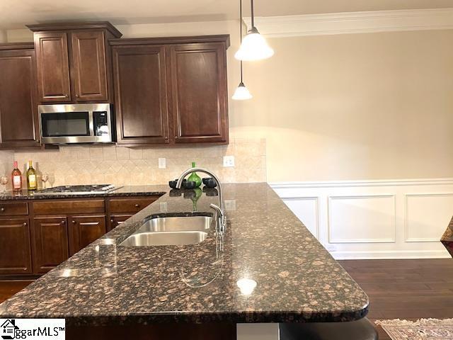 kitchen with sink, hanging light fixtures, dark stone countertops, dark brown cabinets, and appliances with stainless steel finishes