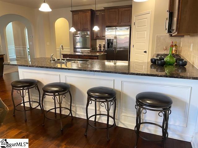 kitchen with pendant lighting, sink, decorative backsplash, appliances with stainless steel finishes, and a kitchen bar