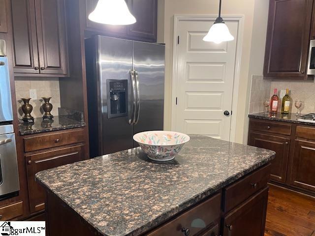 kitchen featuring backsplash, a kitchen island, stainless steel refrigerator with ice dispenser, and hanging light fixtures