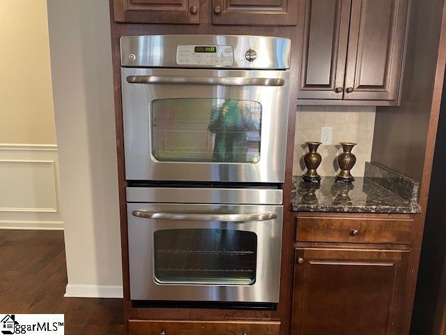 kitchen with dark brown cabinetry, dark hardwood / wood-style floors, double oven, and dark stone counters