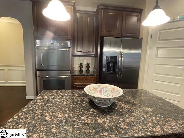 kitchen with dark stone counters, decorative light fixtures, decorative backsplash, dark brown cabinets, and stainless steel appliances