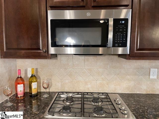 kitchen featuring dark brown cabinetry, stainless steel appliances, tasteful backsplash, and dark stone counters