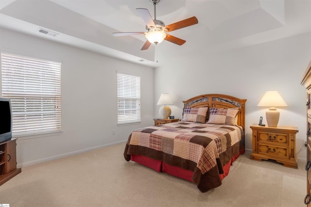 bedroom featuring light colored carpet, a raised ceiling, and ceiling fan