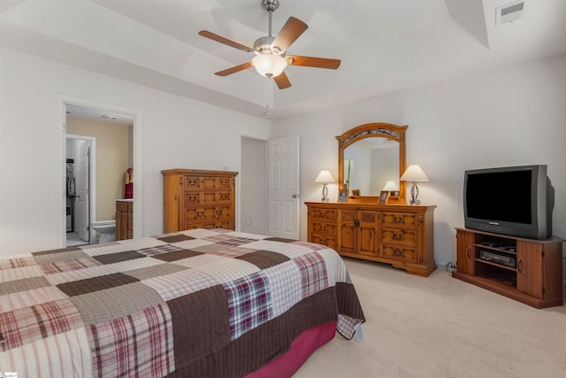 carpeted bedroom with a raised ceiling, connected bathroom, and ceiling fan