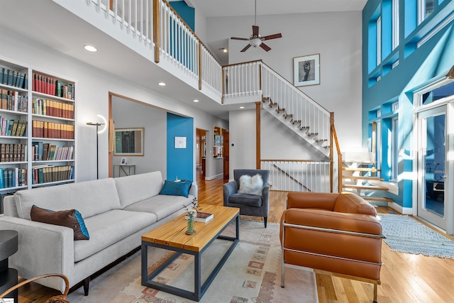 living room featuring ceiling fan, a towering ceiling, and light hardwood / wood-style flooring