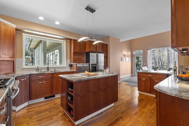 kitchen with light stone countertops, decorative backsplash, stainless steel appliances, a kitchen island, and hanging light fixtures