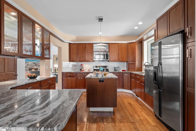 kitchen with tasteful backsplash, light stone counters, stainless steel appliances, a kitchen island, and hanging light fixtures