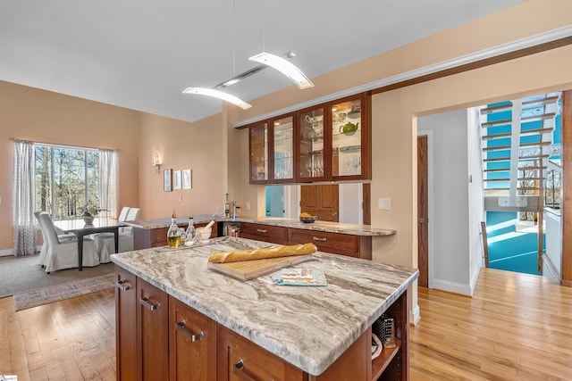 kitchen with kitchen peninsula, light stone counters, pendant lighting, light hardwood / wood-style floors, and a kitchen island