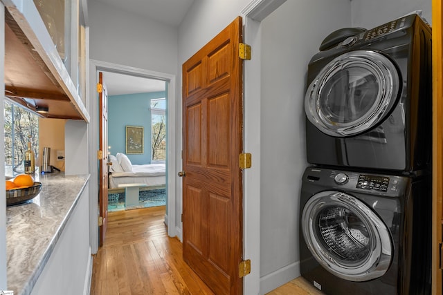 clothes washing area featuring stacked washer / dryer, a wealth of natural light, and light wood-type flooring