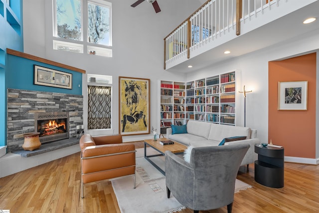 living room featuring light wood-type flooring, a towering ceiling, a stone fireplace, and ceiling fan