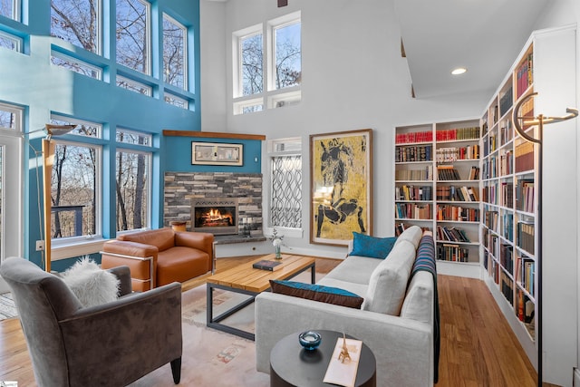 living room featuring a stone fireplace, built in shelves, light hardwood / wood-style floors, and a high ceiling