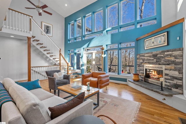 living room featuring ceiling fan, a fireplace, a towering ceiling, and light wood-type flooring