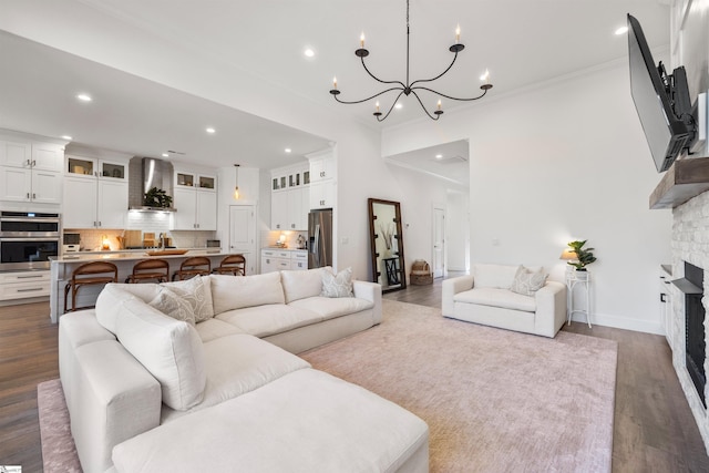 living room with a chandelier, a stone fireplace, crown molding, and dark wood-type flooring