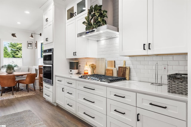 kitchen featuring light wood-type flooring, tasteful backsplash, wall chimney exhaust hood, stainless steel appliances, and white cabinets