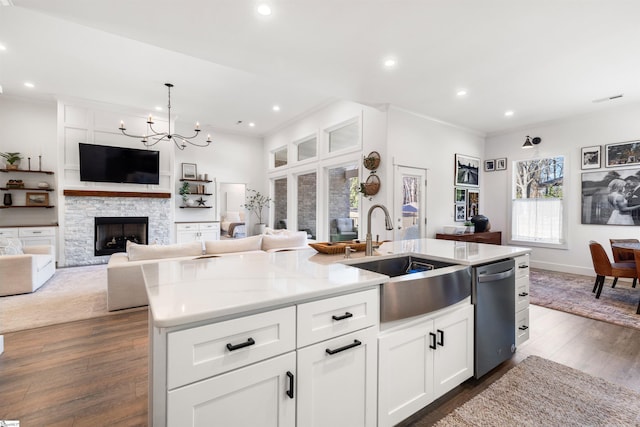 kitchen featuring stainless steel dishwasher, a kitchen island with sink, sink, a fireplace, and white cabinetry