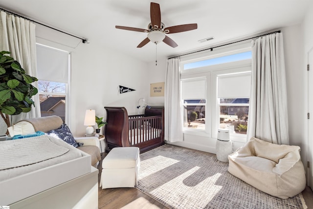 bedroom featuring a nursery area, light hardwood / wood-style floors, and ceiling fan