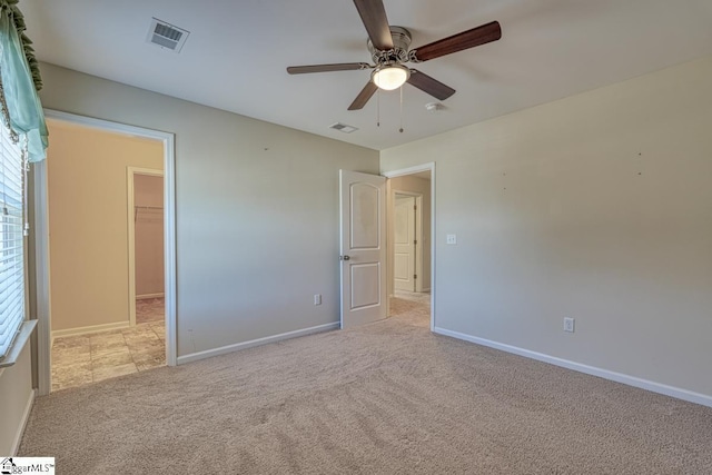 unfurnished bedroom with light carpet, a walk in closet, a closet, and ceiling fan