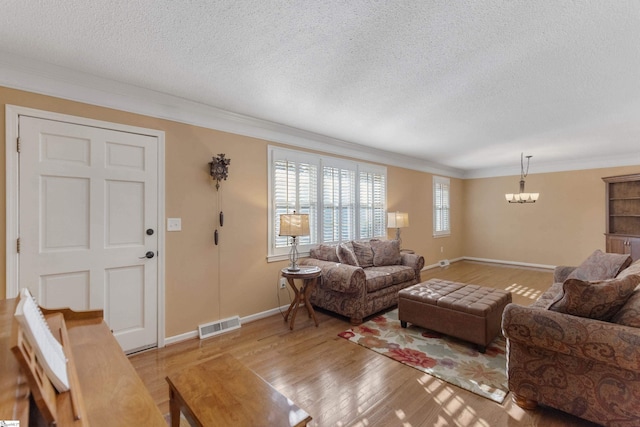 living room featuring crown molding, light hardwood / wood-style floors, a textured ceiling, and a notable chandelier