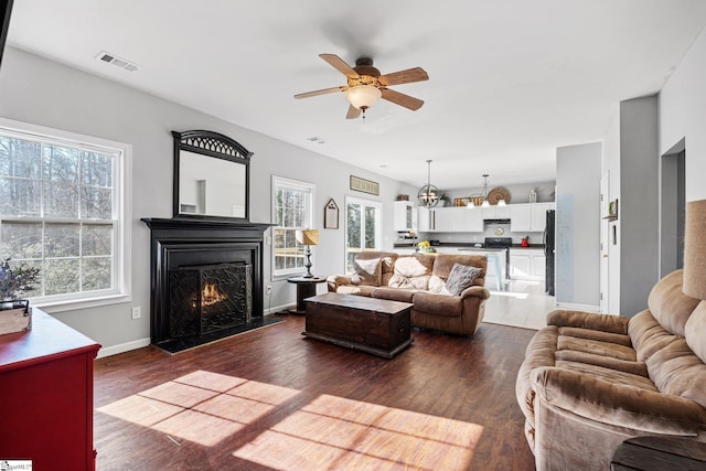 living room with plenty of natural light, dark wood-type flooring, and ceiling fan